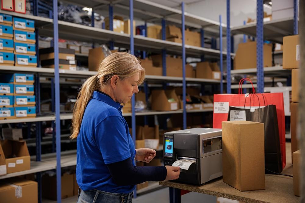 En lagerarbeider bruker en industriell etikettskriver for å skrive ut etiketter til pakker på et lager.