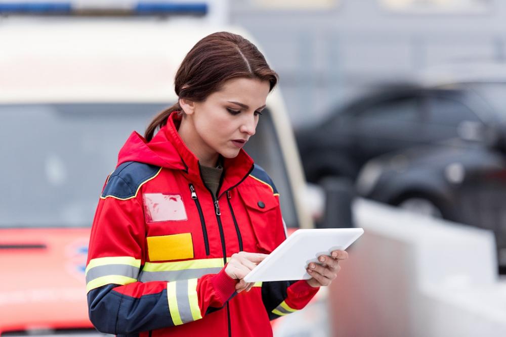 En kvinnelig ambulansearbeider i rød uniform sjekker informasjon på et nettbrett administrert av SOTI MobiControl